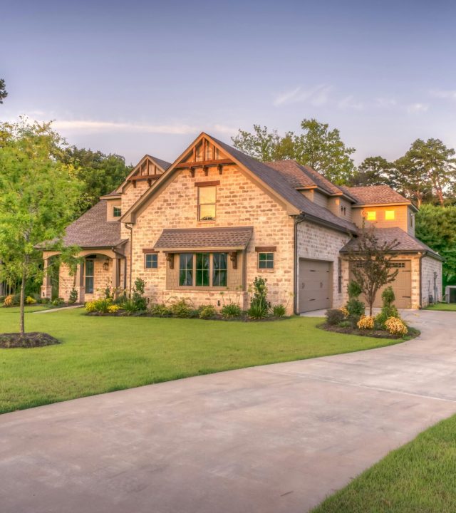 Elegant stone family home surrounded by trees, lush lawn, and vibrant garden.